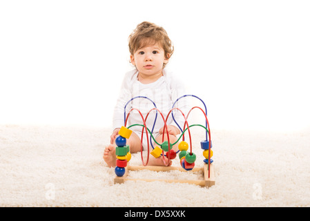 Surprised toddler boy sitting on fur carpet and playing with wooden toy against white background Stock Photo