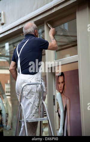 Senior Man on Ladder Painting Store Door Framework in Richmond London UK Stock Photo