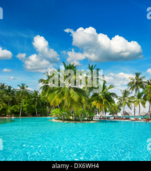 swimming pool surrounded by lush tropical plants and palm trees over blue cloudy sky Stock Photo