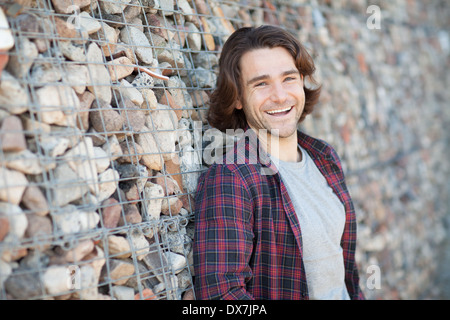 A relaxed young man pictured outdoors next to a wall made from stones Stock Photo