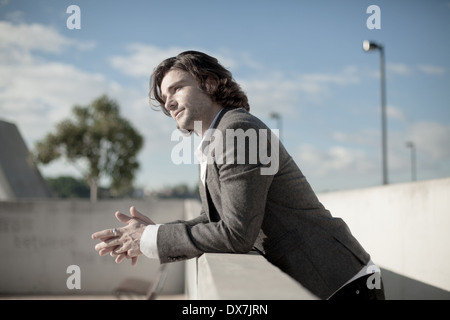 A young male model leaning against a wall with a blue sky behind him Stock Photo