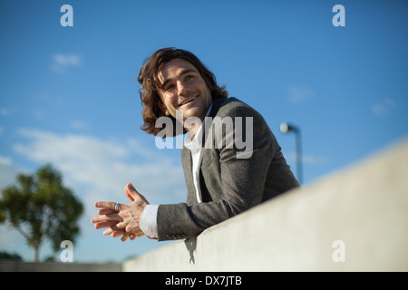 A young male model leaning against a wall with a blue sky behind him Stock Photo