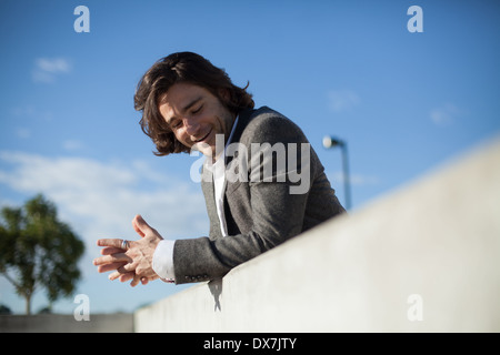 A young male model leaning against a wall with a blue sky behind him Stock Photo