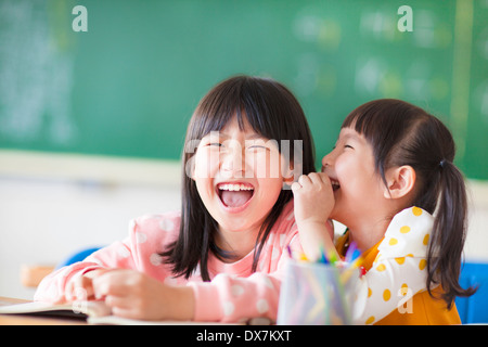 Laughing little girls sharing secrets in class Stock Photo