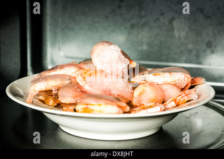 Frozen shrimp covered with a thick layer of ice. In the microwave. Stock Photo