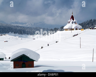 India, Kashmir, Gulmarg, Himalayan Ski Resort, men walking to snow laden Maharani Shiv Ji Temple Stock Photo