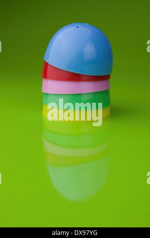Five half shell plastic Easter egg shells, on a glossy green background, with reflection, blue, red, pink, green and yellow Stock Photo