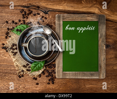 cup of coffee and antique blackboard with sample text bon appetit. coffee leaves and beans Stock Photo