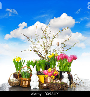 spring flowers with easter bunny and eggs decoration. tulips, snowdrops and narcissus blooms over blue sky background Stock Photo