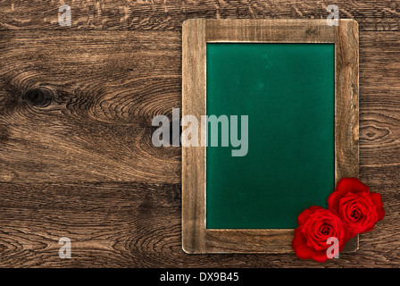 blank vintage green blackboard with rustic frame and red roses on wooden background Stock Photo
