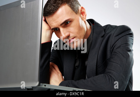 Thoughtful businessman sitting at the table with laptop on gray backgorund Stock Photo