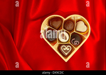 delicious chocolate pralines in golden heart shape gift box on red satin background