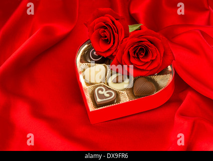 red roses and assorted chocolate pralines in golden heart shaped gift box on satin background