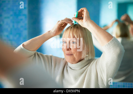 old caucasian woman applying lotion to prevent hair loss, looking at mirror in bathroom Stock Photo