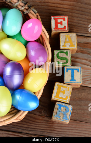 The word Easter spelled out in childrens toy blocks and a Basket full of plastic eggs. Vertical format on a rustic wood table. Stock Photo