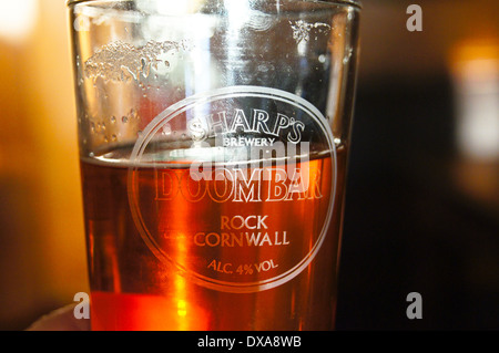 A partly empty printed glass of Sharps Doom Bar real ale backlit in an engraved glass, pub table drinks glasses Stock Photo