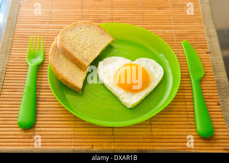 Fried egg in heart shape on green plastic plate Stock Photo
