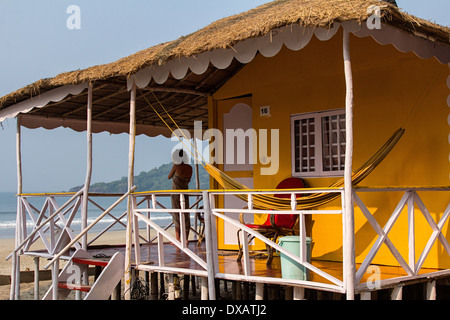 Woman standing on the porch of a bright yellow beach hut with a hammock at Palolem Beach in Goa, India Stock Photo