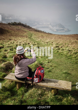 A woman taking a photograph of Ilfracombe harbor as the morning mist starts to lift
