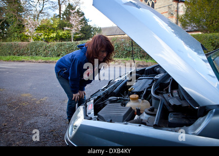 Woman looking under bonnet of broken down car Stock Photo