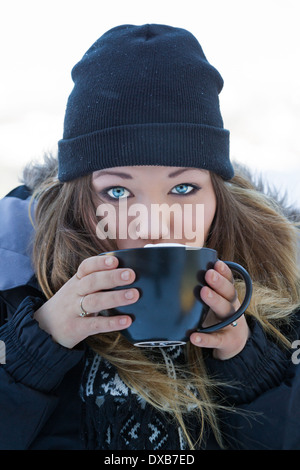 attractive young woman with beautiful blue eyes drinking hot chocolate outdoors in snowy winter conditions Stock Photo