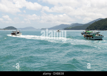 Typical small fishing boat in South Korea with people on board and coastal landscape in the background Stock Photo