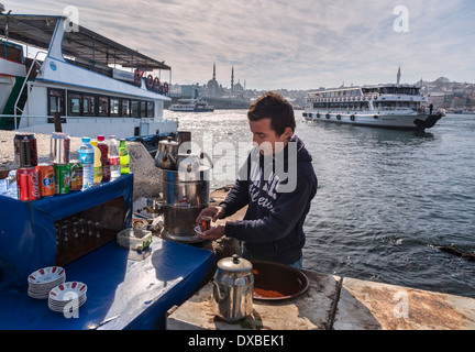 A tea vendor on Karakoy waterfront with the Golden Horn, Yeni mosque at  Eminonu and Istanbul skyline in the background, Turkey. Stock Photo