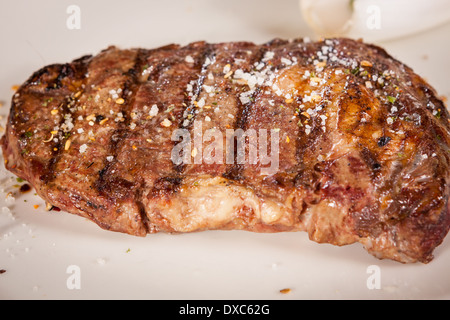 Delicious trimmed lean portion of thick grilled beef steak with seasoning served on a white plate, close up with shallow dof Stock Photo