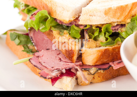 Delicious thinly sliced beef pastrami club sandwich with fresh curly lettuce served with a small dish of pickled vegetables on a white plate, isolated on white Stock Photo