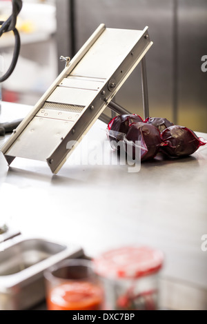 Chef wearing gloves to prevent from the juice from staining his hands slicing boiled beetroot for salads on a metal slicer at a Stock Photo