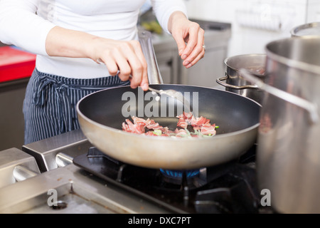 Chef or cook braising meat in a non-stick frying pan over a gas hob as she prepares a meal in a commercial restaurant kitchen