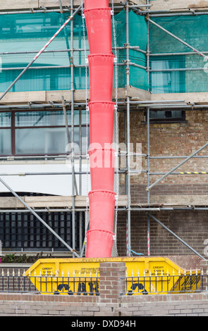 Red rubbish chute going into a yellow skip on some scaffolding on a tall building. Stock Photo