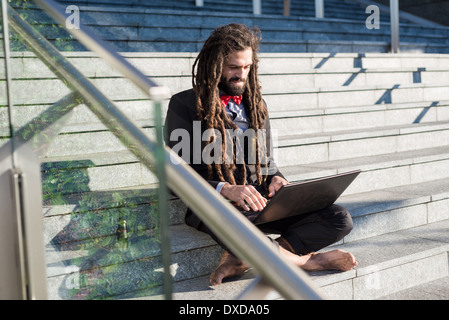 Stylish elegant dreadlocks businessman using notebook in business landscape Stock Photo