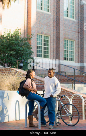 Young man and young woman outdoors on college campus, talking next to bike rack, Florida, USA Stock Photo