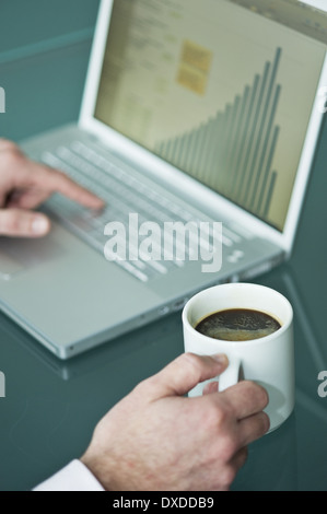 Businessman's hands with coffee cup at laptop with bar chart Stock Photo