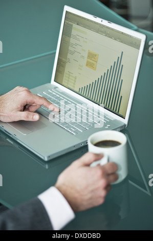 Businessman's hands with coffee cup at laptop with bar chart Stock Photo