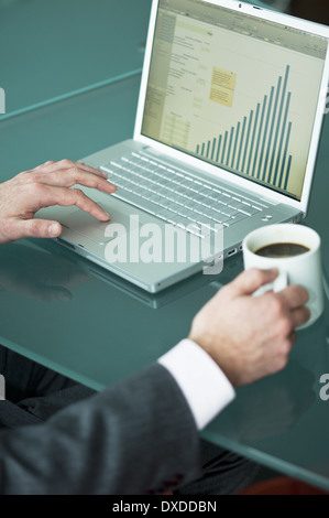 Businessman's hands with coffee cup at laptop with bar chart Stock Photo