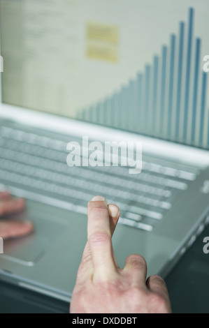 Businessman's fingers crossed at laptop with bar chart Stock Photo