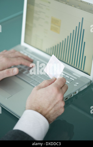 Businessman's hands holding credit card at laptop with bar chart Stock Photo