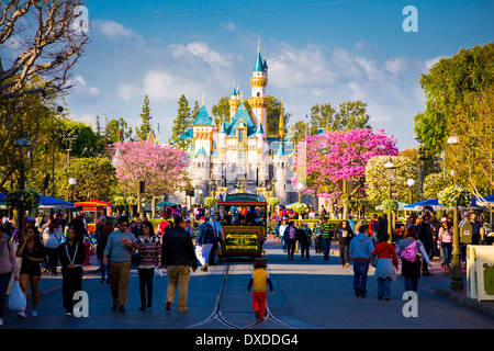 Disneyland Main Street crowded with guests and a tram car in the road leading towards the iconic pink castle. Stock Photo