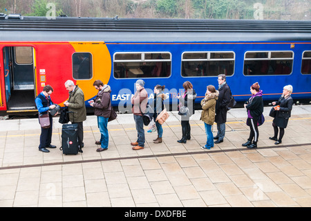 A queue of train passengers getting tickets from a train guard on the platform at Leicester station before boarding an East Midlands Train Stock Photo