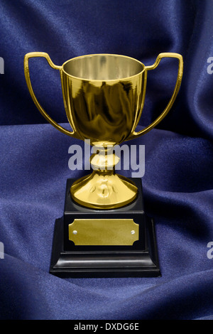A Gold Winners trophy on a blue silk background great concept for achievement, success or winning a competition or award. Stock Photo