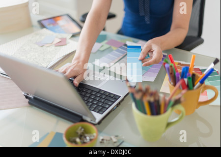 Woman holding color swatches and using laptop Stock Photo