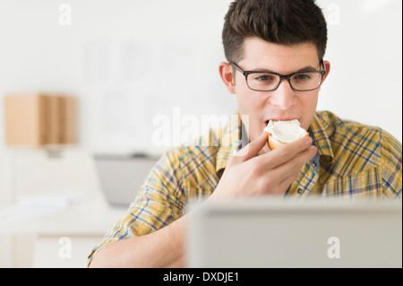 Young man eating sandwich and using laptop Stock Photo
