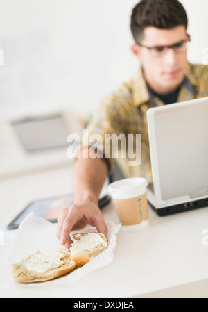 Young man eating sandwich and using laptop Stock Photo