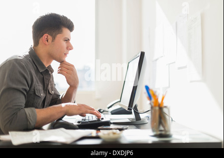 Young man using computer, hand on chin Stock Photo - Alamy