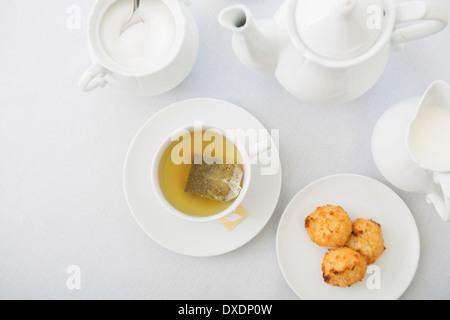 Cup of tea in porcelain white teacup with saucer, sugar bowl, creamer, teapot and plate of coconut macaroons, studio shot Stock Photo