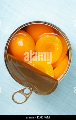 Open can of apricots, on blue background, studio shot Stock Photo