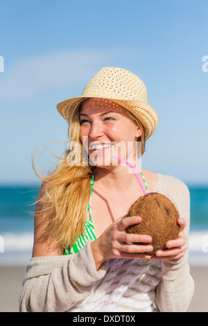 Young woman on beach drinking coconut juice, Jupiter, Florida, USA Stock Photo