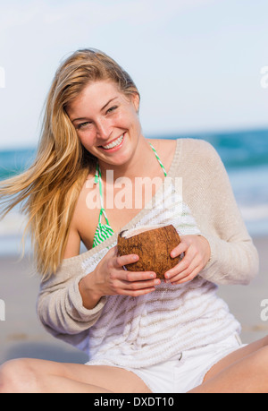 Young woman on beach drinking coconut juice, Jupiter, Florida, USA Stock Photo